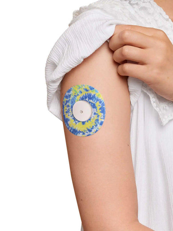 Colorful Freestyle Libre 2 patch with blue and yellow tie-dye design on arm, secure and stylish.