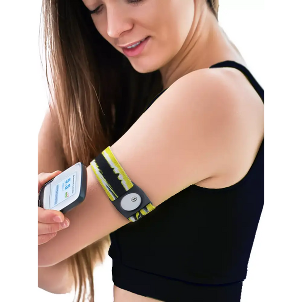 Woman wearing a yellow and black Freestyle Libre 3 Arm Band on upper arm while checking glucose monitor reading